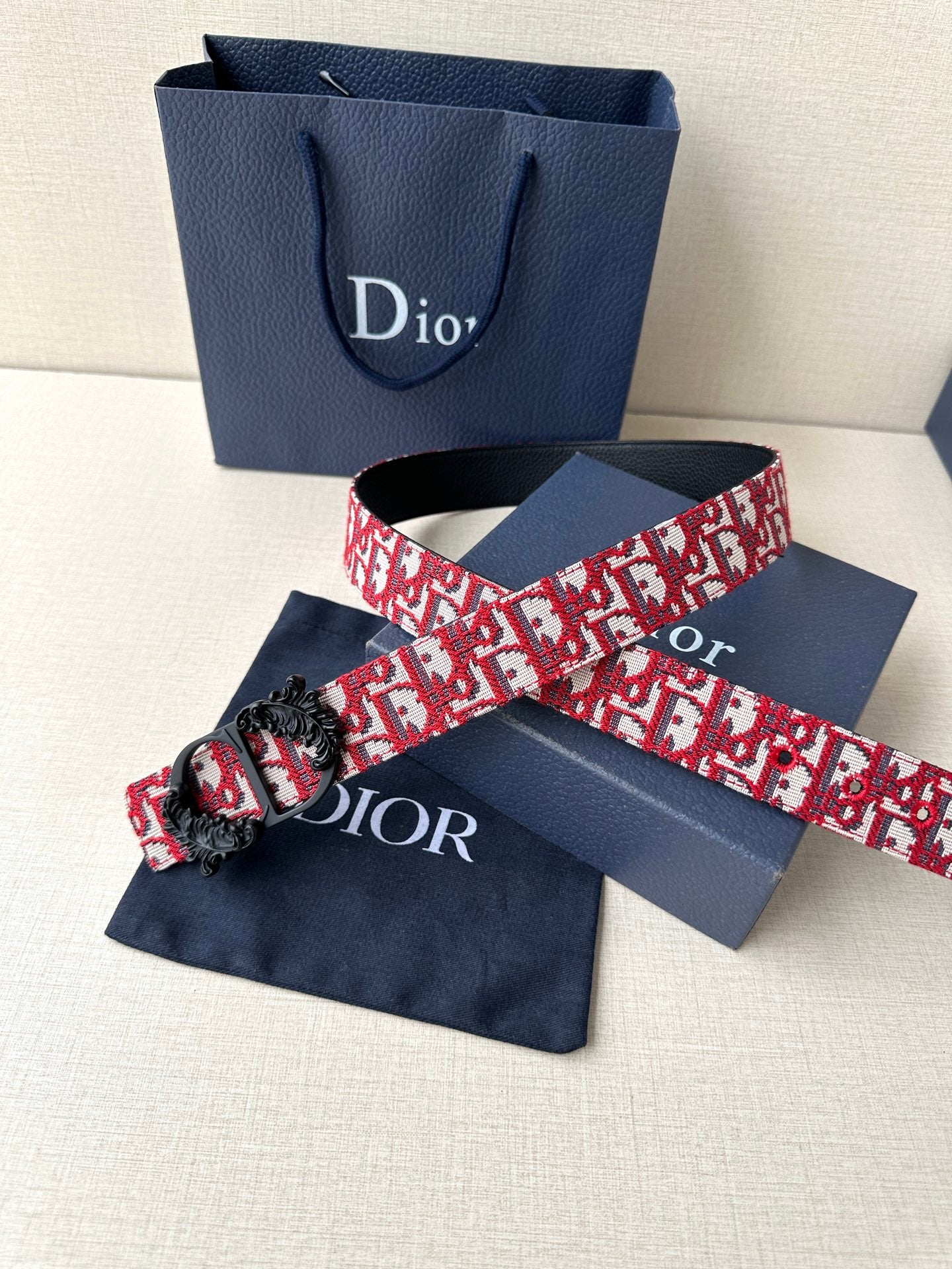 Dior belt flat lay with red-and-white monogram pattern and black ornate clasp.