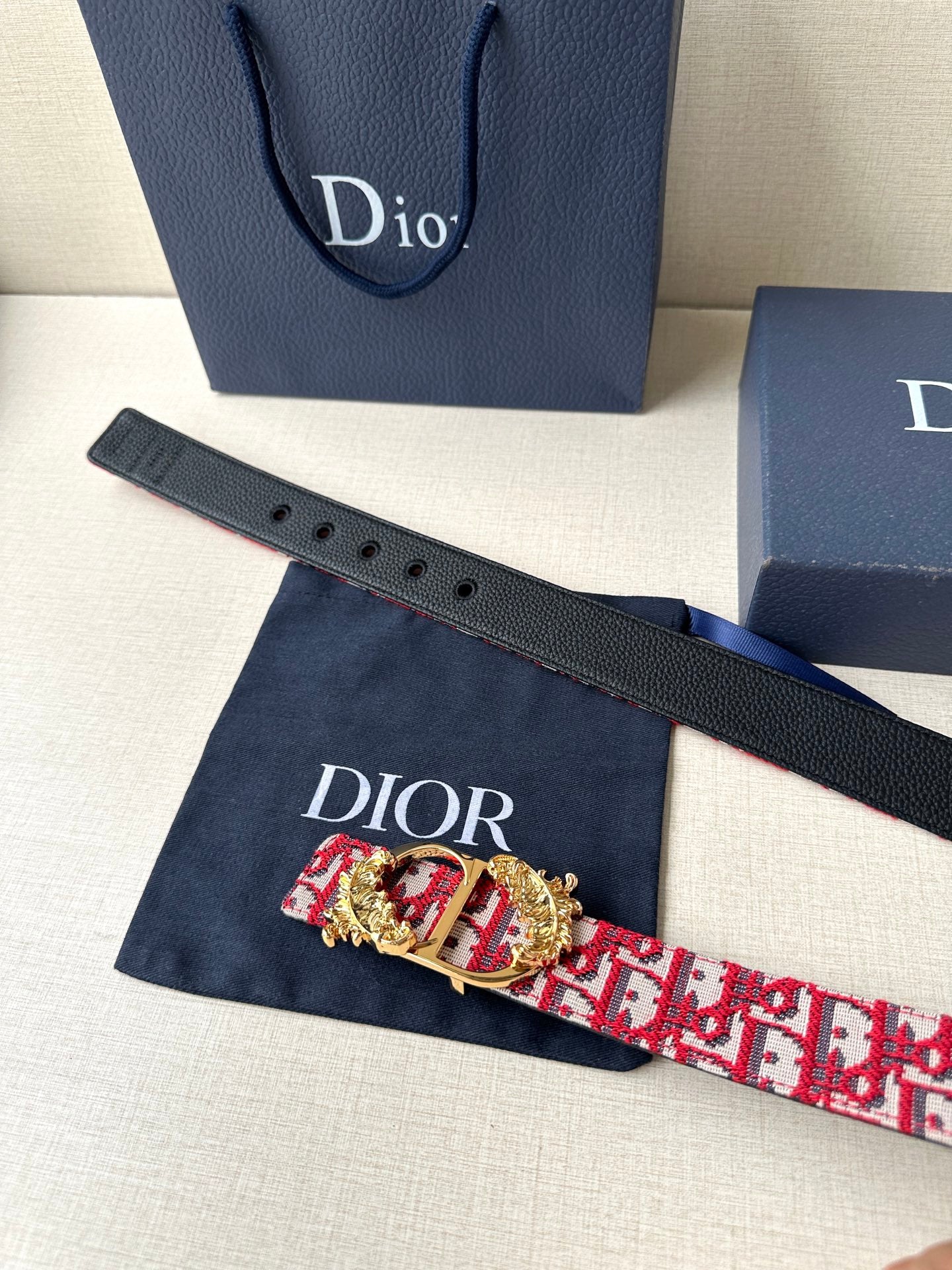 Black leather strap belt with red monogram section and gold-tone buckle