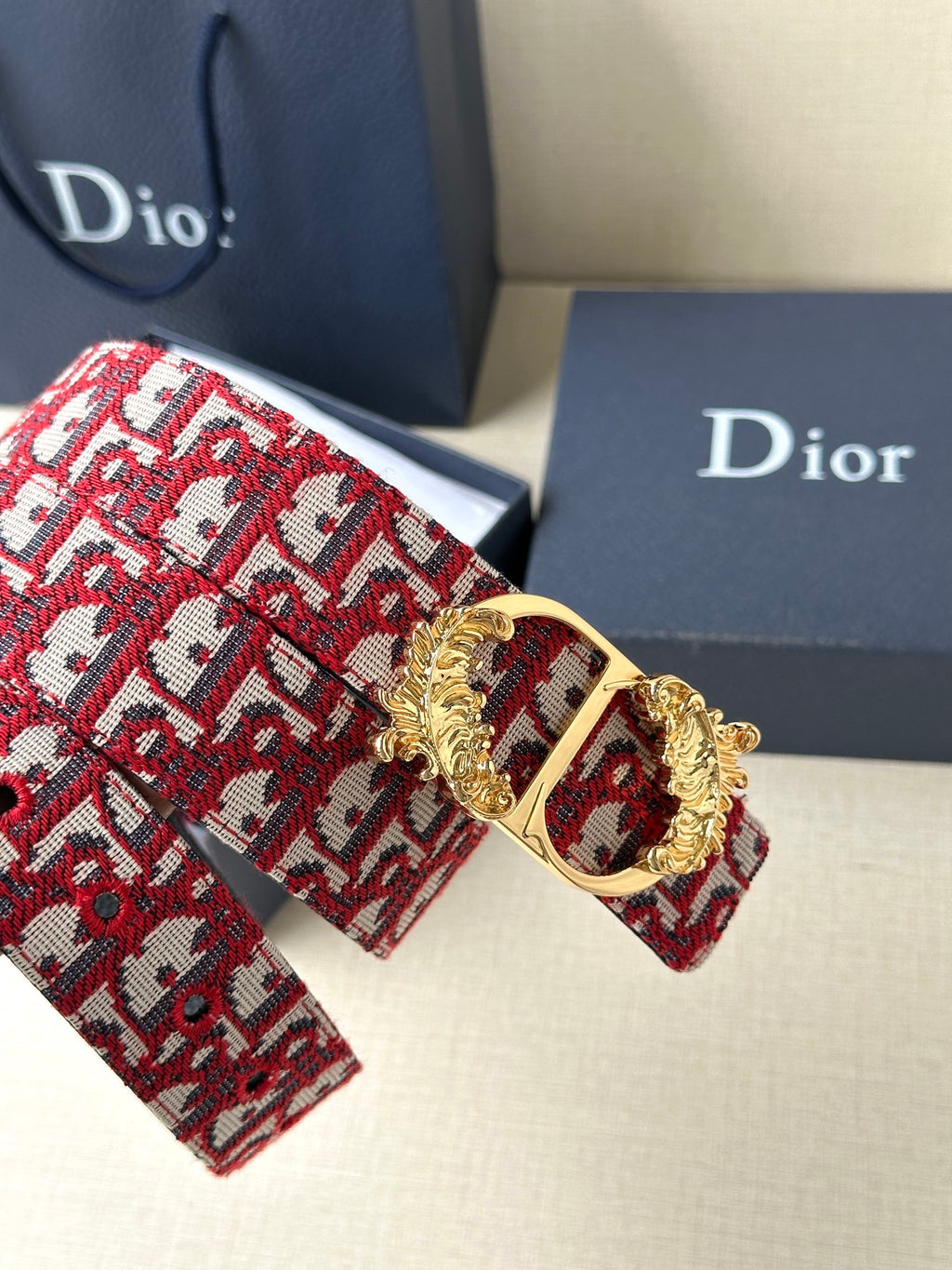 Red monogram belt detail with gold buckle frame and ornate crest centerpiece