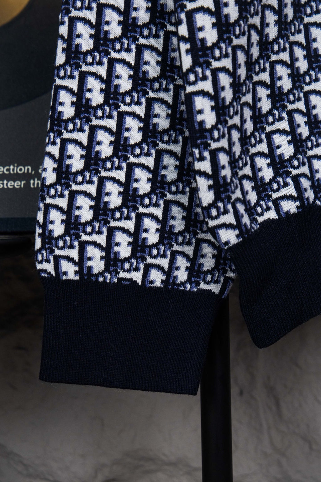 Sleeve and hem detail of knit sweater with monogram pattern and navy cuffs