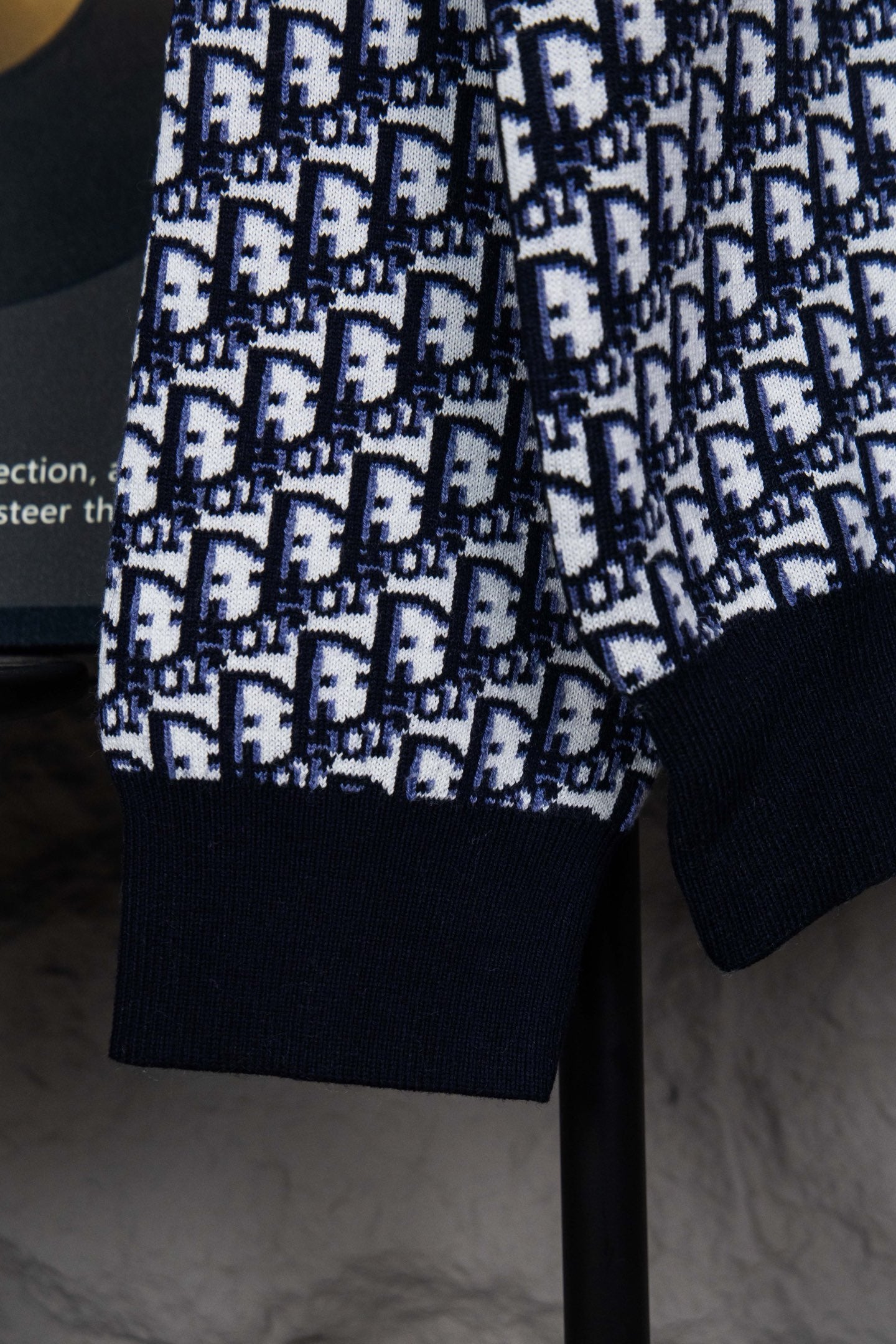 Sleeve and hem detail of knit sweater with monogram pattern and navy cuffs