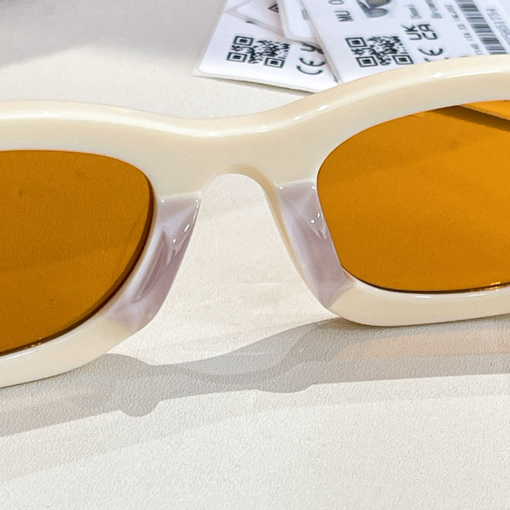 MiuMiu cream sunglasses close-up with amber lenses and gold-tone bridge detail