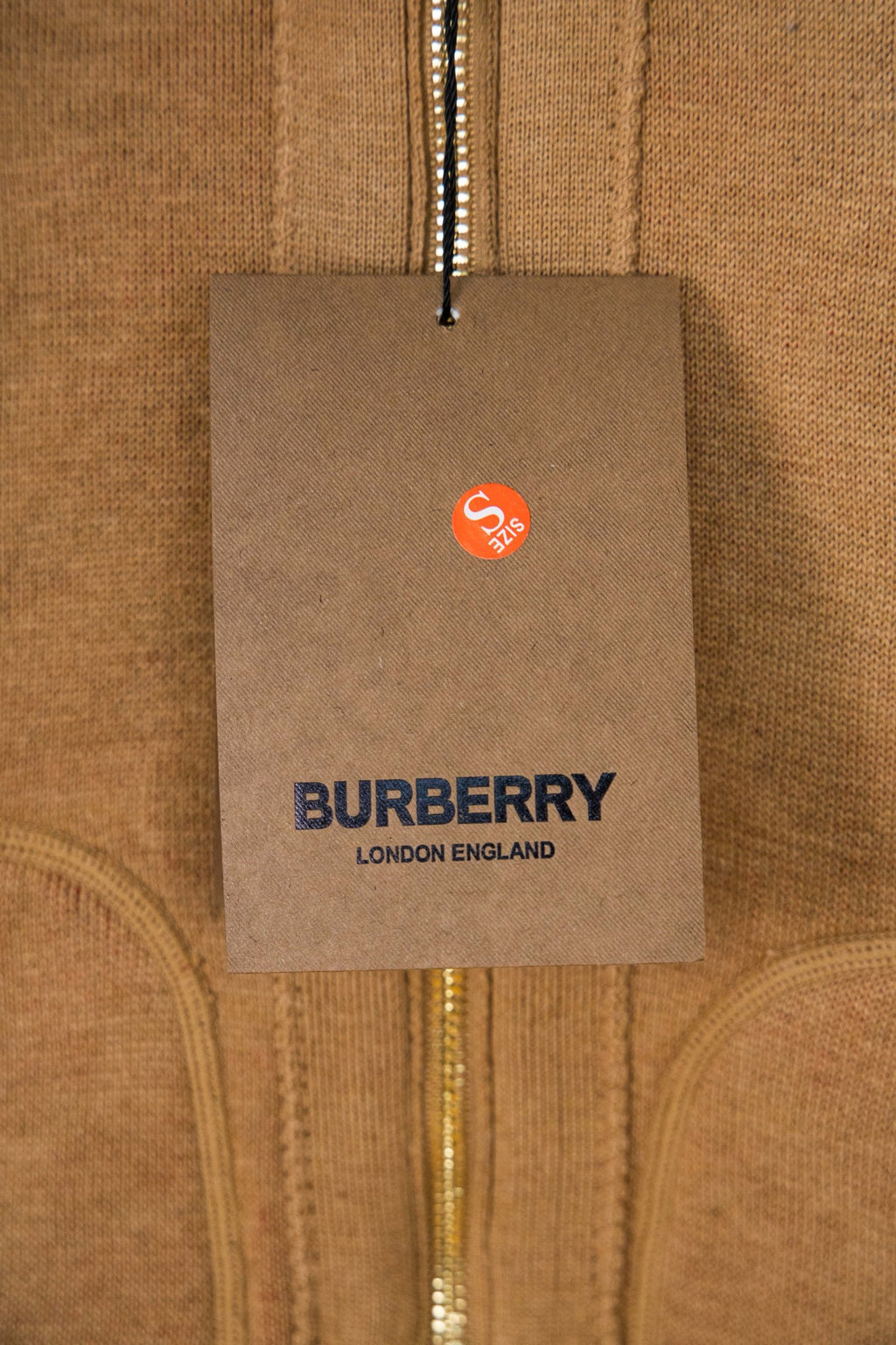 Burberry logo clothing hang tag attached to tan knit jacket