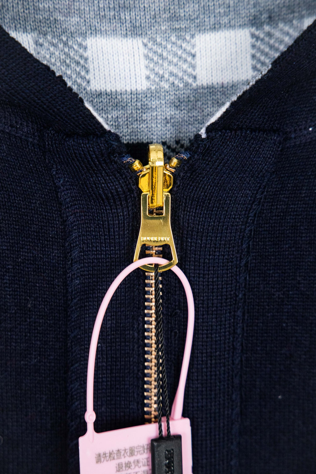 Navy hooded zip-up jacket close-up with gold zipper and pale pink loop pull