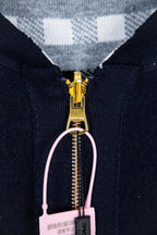 Navy hooded zip-up jacket close-up with gold zipper and pale pink loop pull