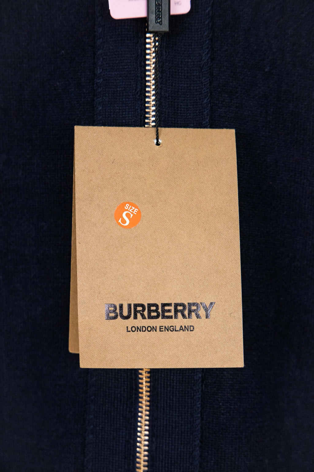 Navy zip-up knit jacket fabric with hanging Burberry logo tag on zipper