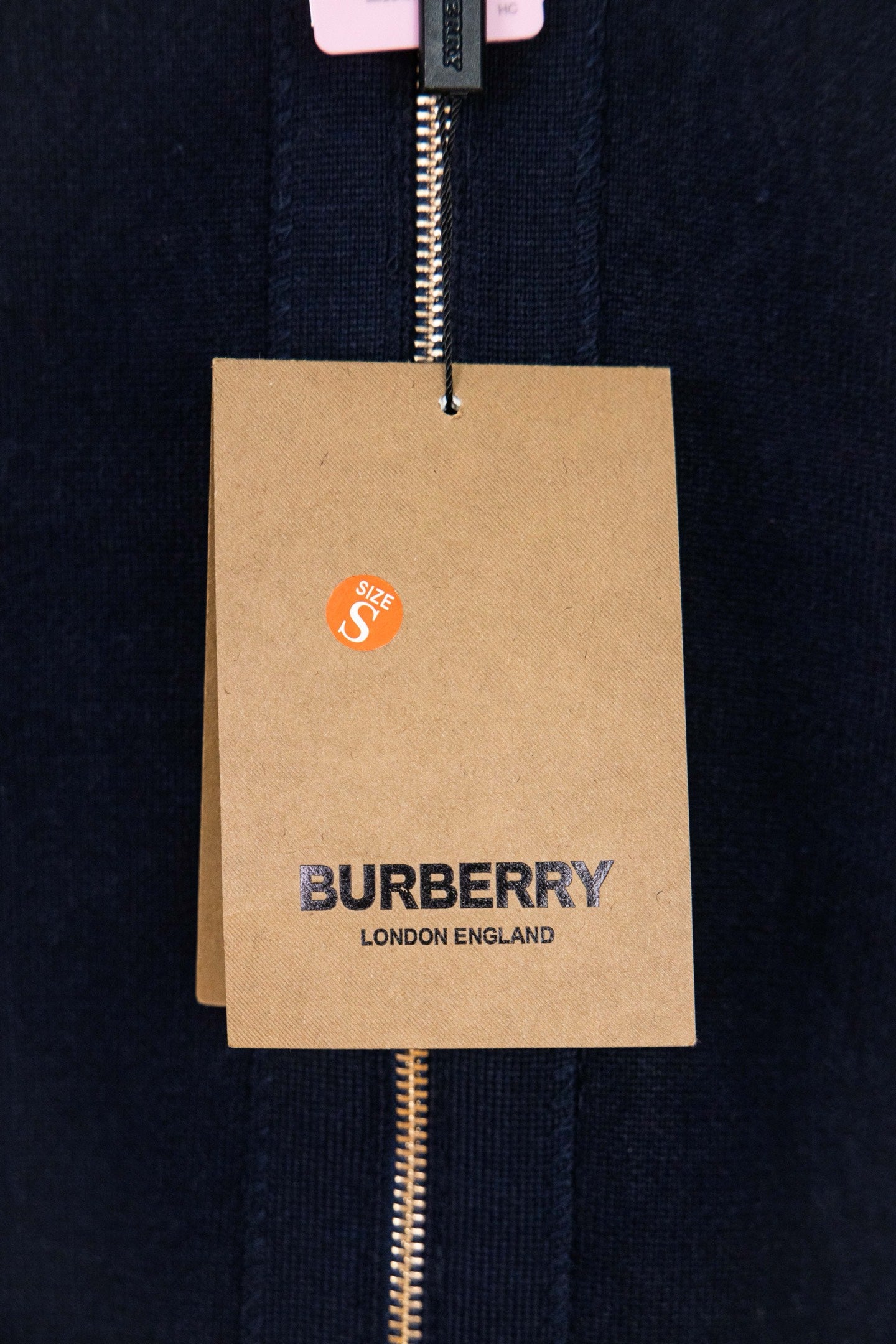Navy zip-up knit jacket fabric with hanging Burberry logo tag on zipper