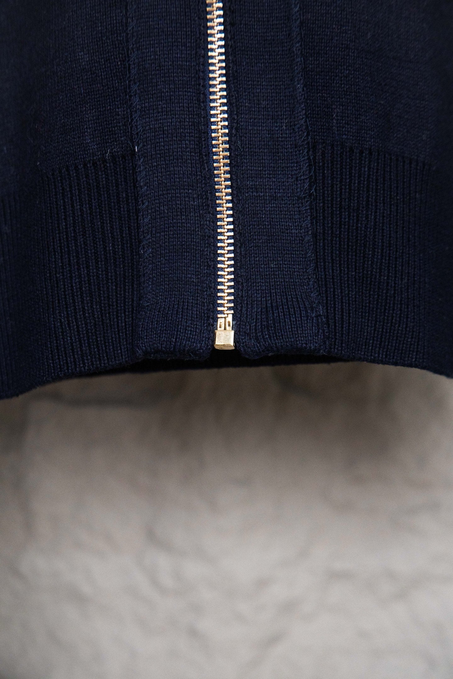 Bottom front close-up of navy hooded zip-up knit jacket with gold zipper teeth