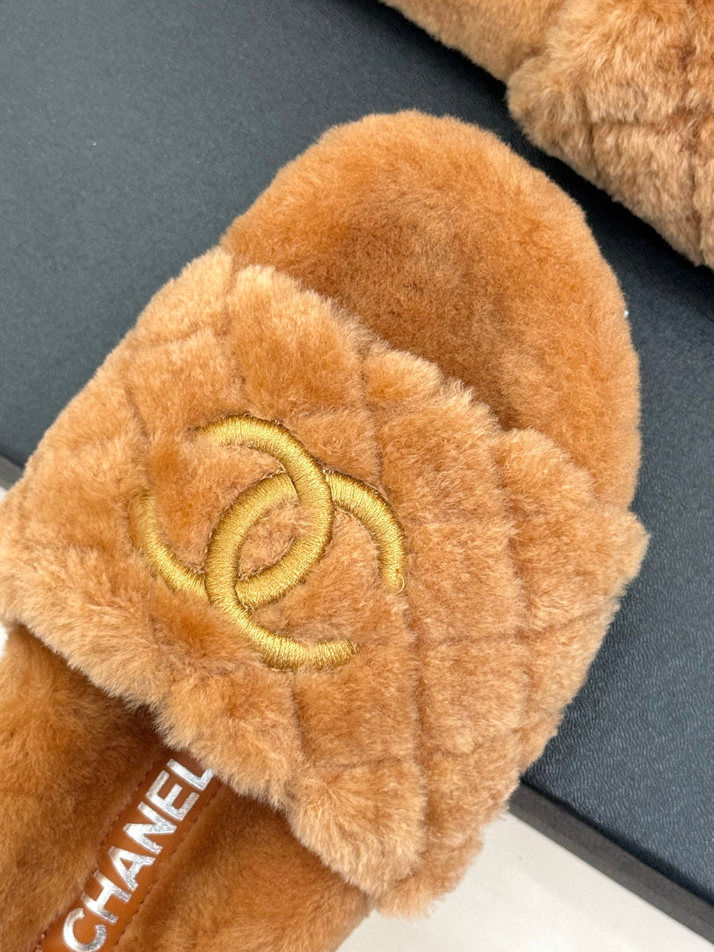 Close-up of tan Chanel fuzzy slide slipper with gold Double C logo on top