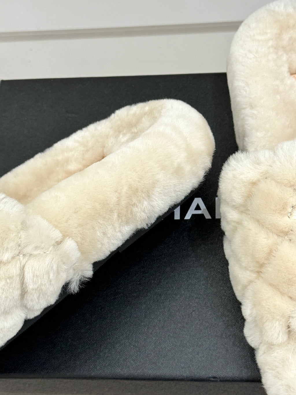 Cream plush slide sandal toe and side view on black display box