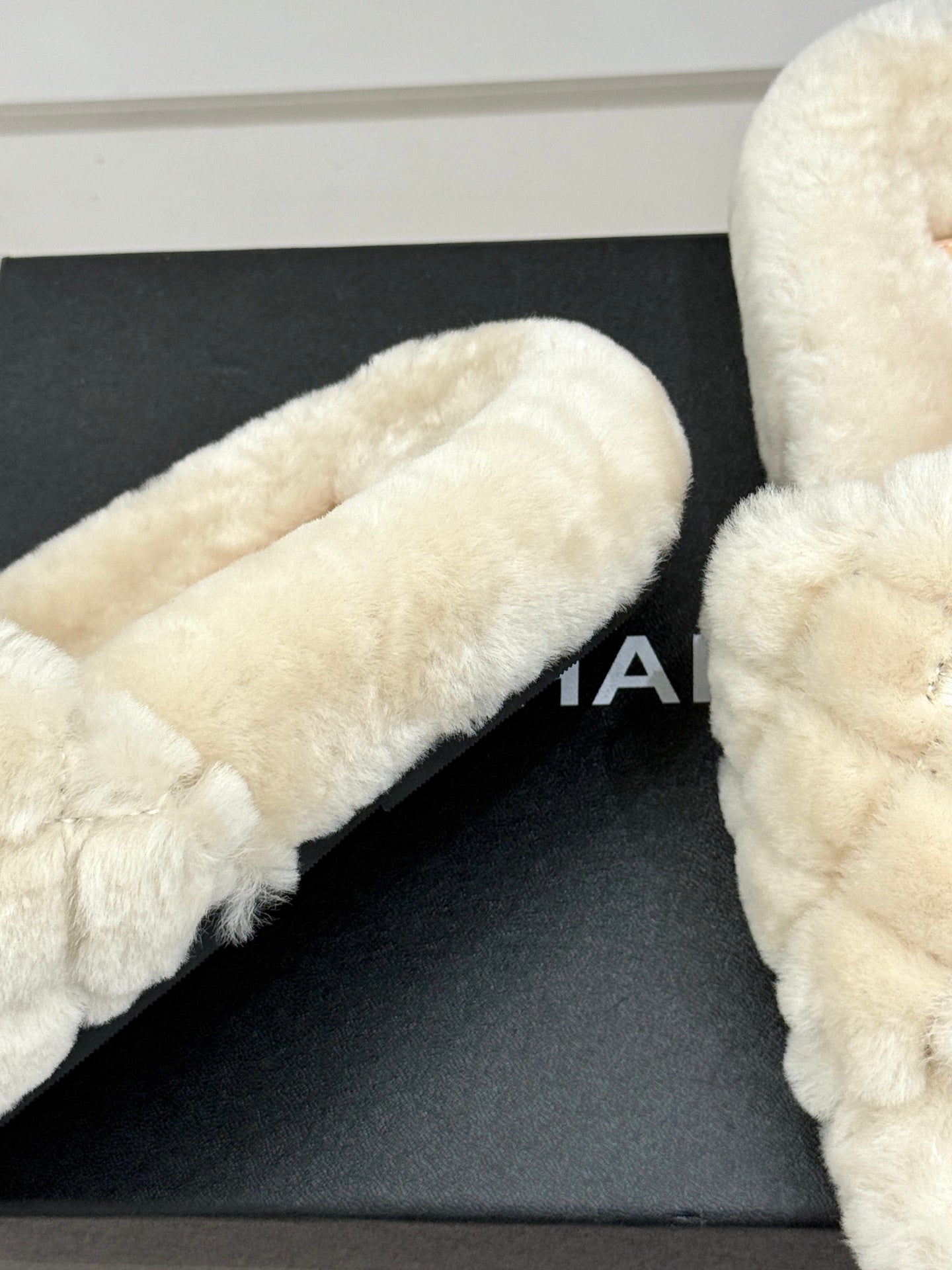 Cream plush slide sandal toe and side view on black display box