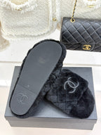 Dark faux-fur Chanel slide with flat sole showing CC logo, on gray box