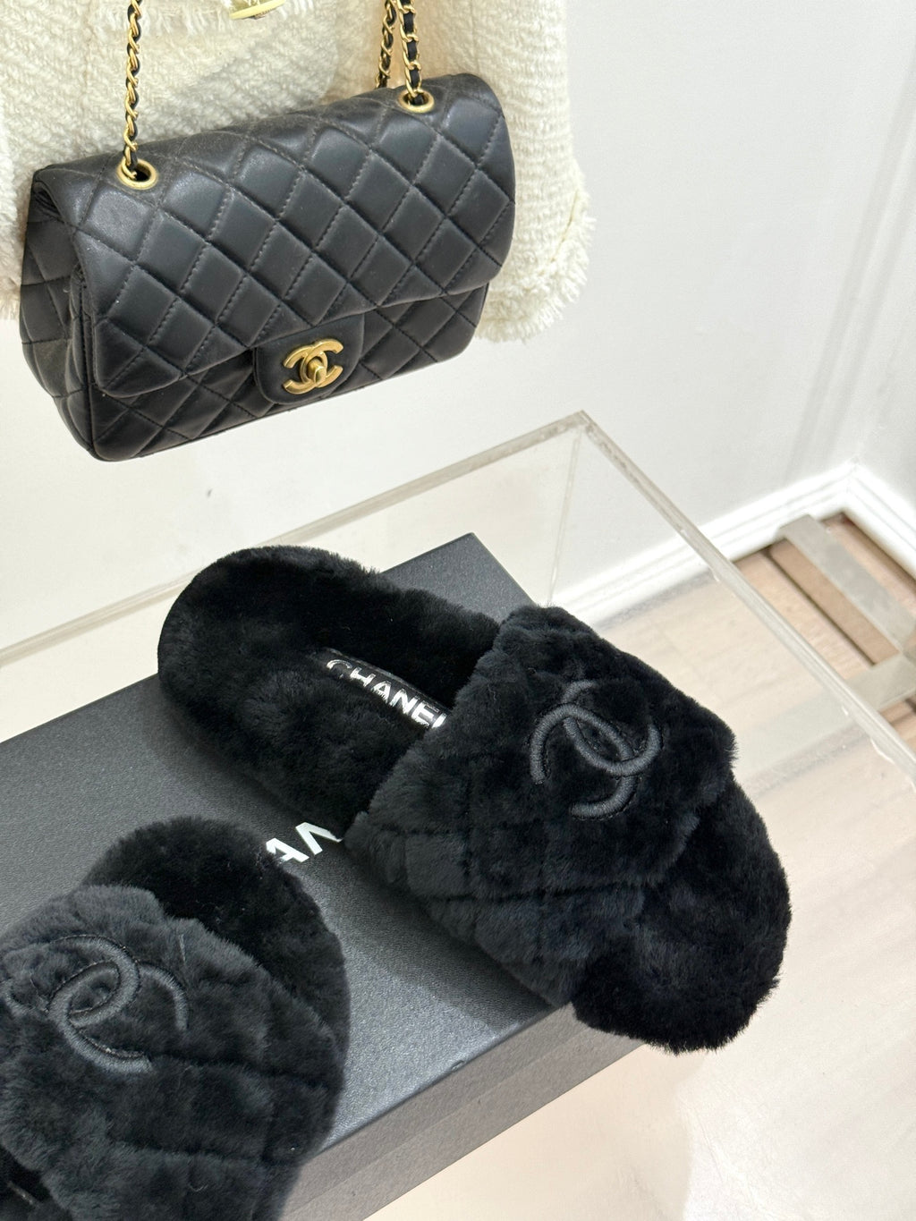 Dark faux-fur Chanel slides on gray box, with black quilted Chanel bag nearby