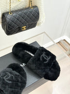 Dark faux-fur Chanel slides on gray box, with black quilted Chanel bag nearby