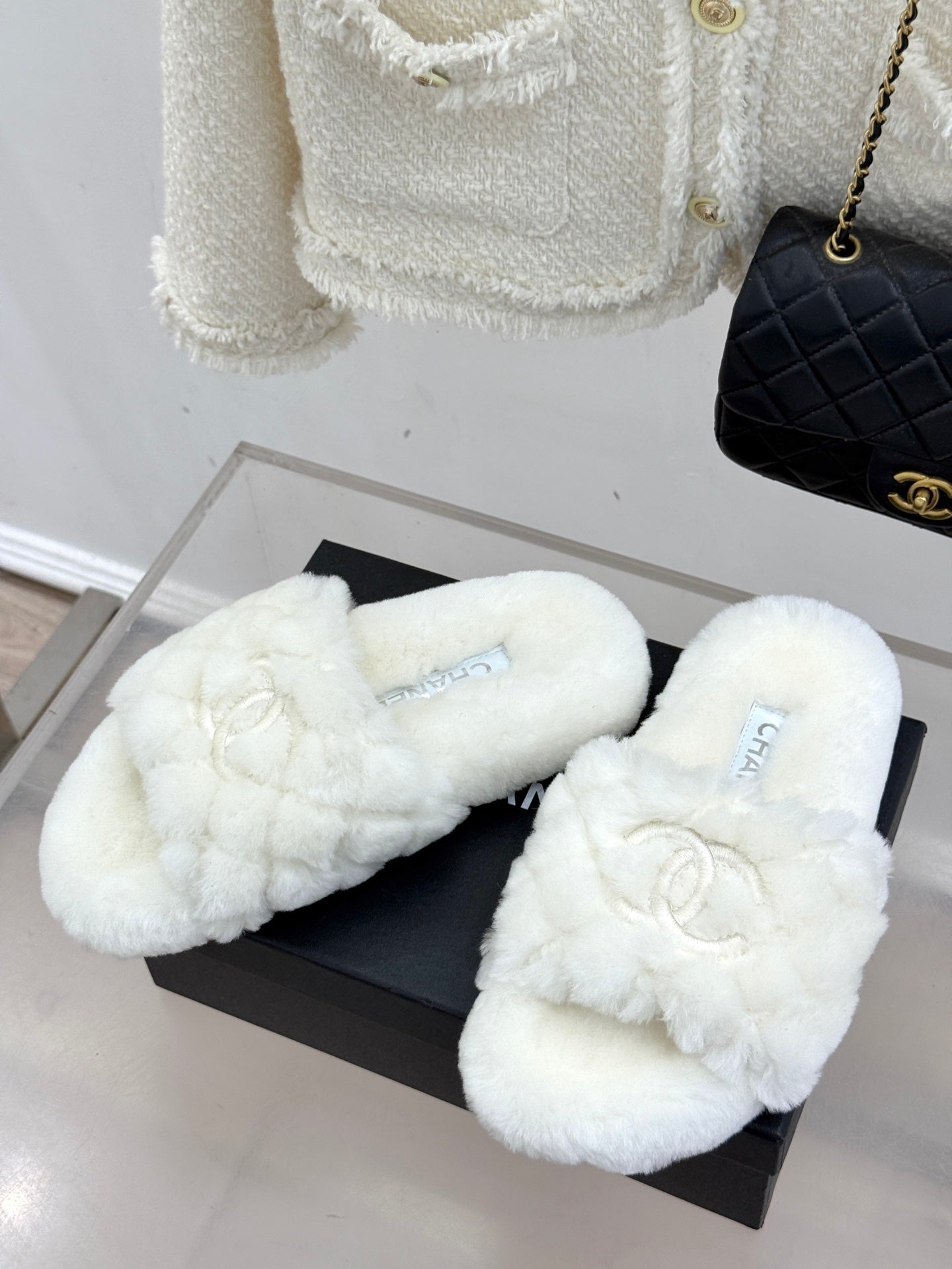 White faux-fur crossband mules with Chanel logo, shown on black box
