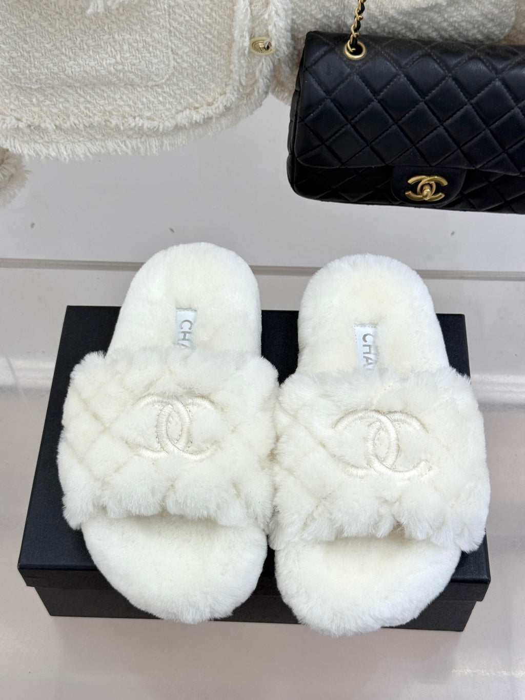 White faux-fur open mules with Chanel logo, displayed on black box