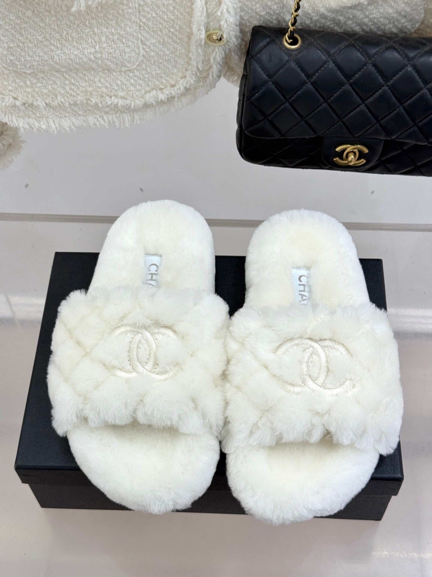 White faux-fur open mules with Chanel logo, displayed on black box