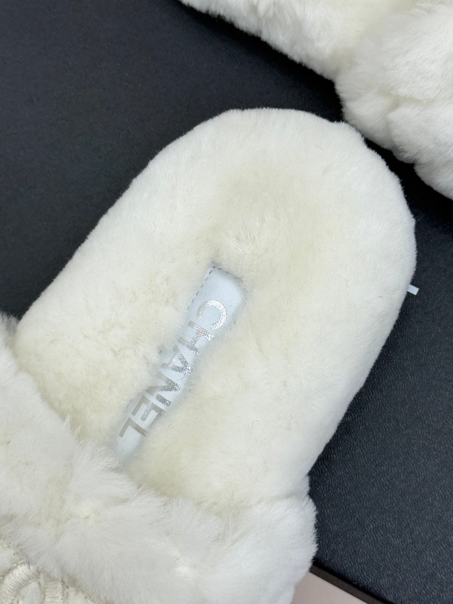 White faux-fur mule with Chanel logo on strap, viewed on black box