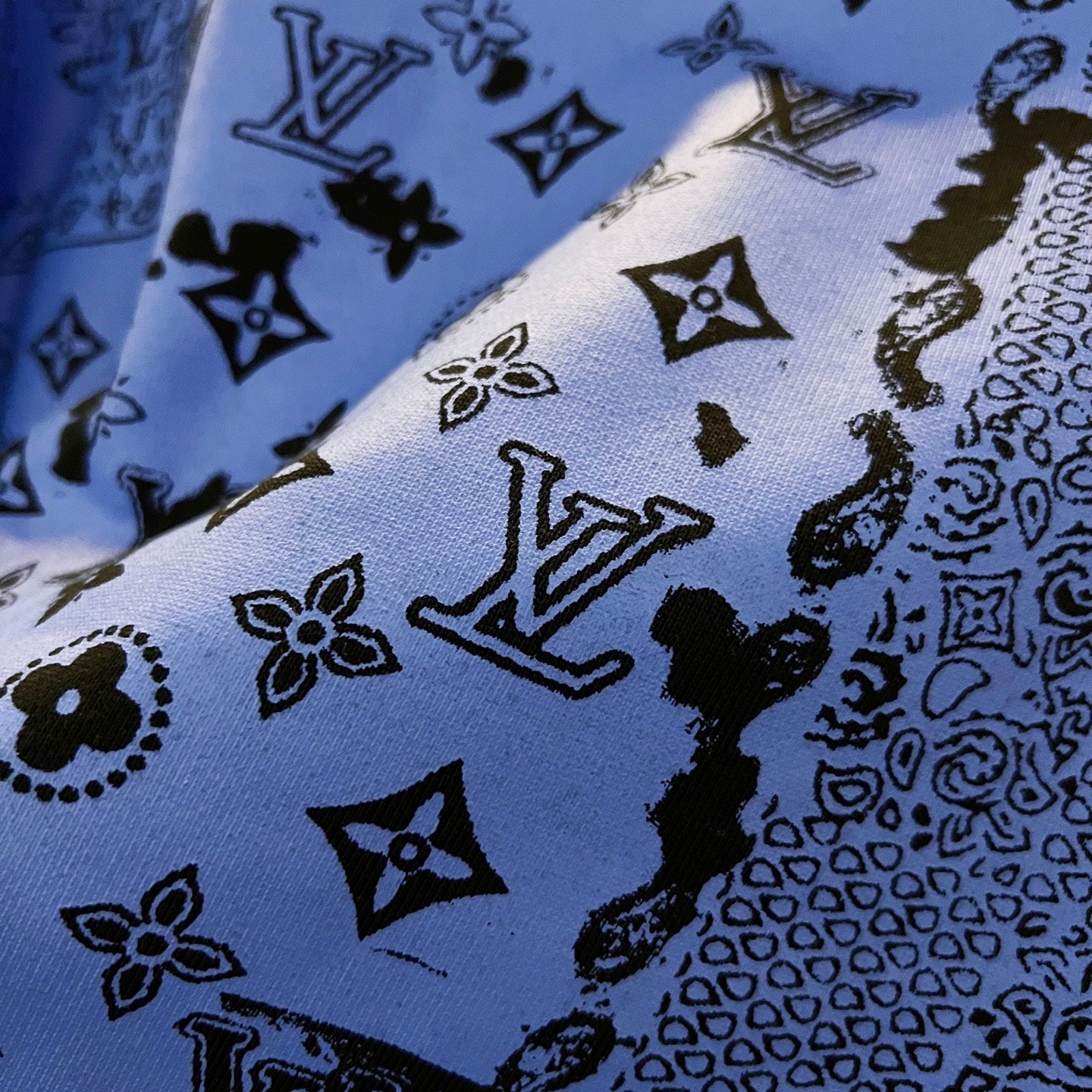 Sweatshirt fabric close-up showing blue ground with black icon and monogram motifs