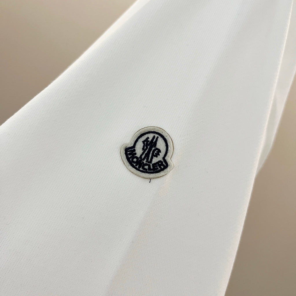 White sweatshirt sleeve with small round Moncler logo patch