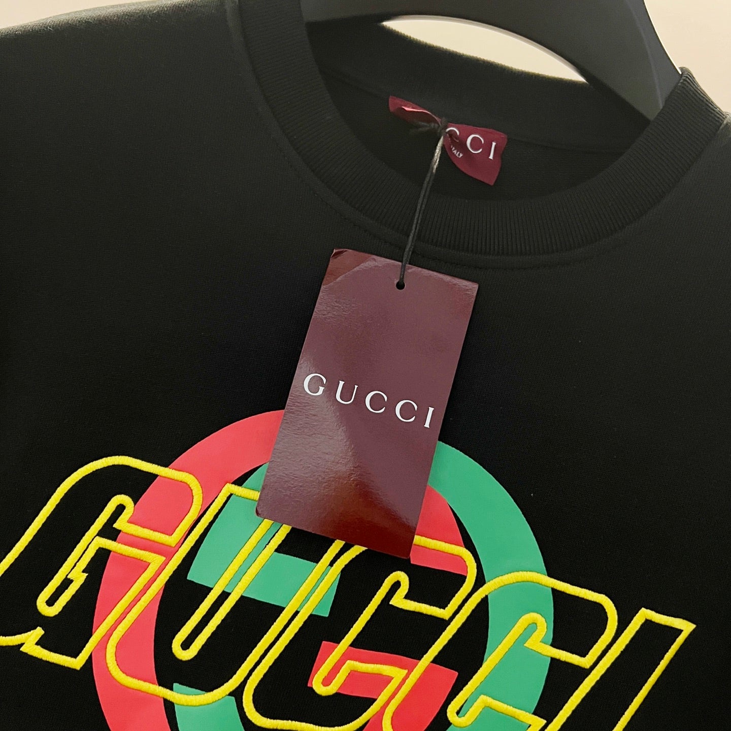 Black sweatshirt with large multicolor GUCCI graphic logo, hanging brand tag.
