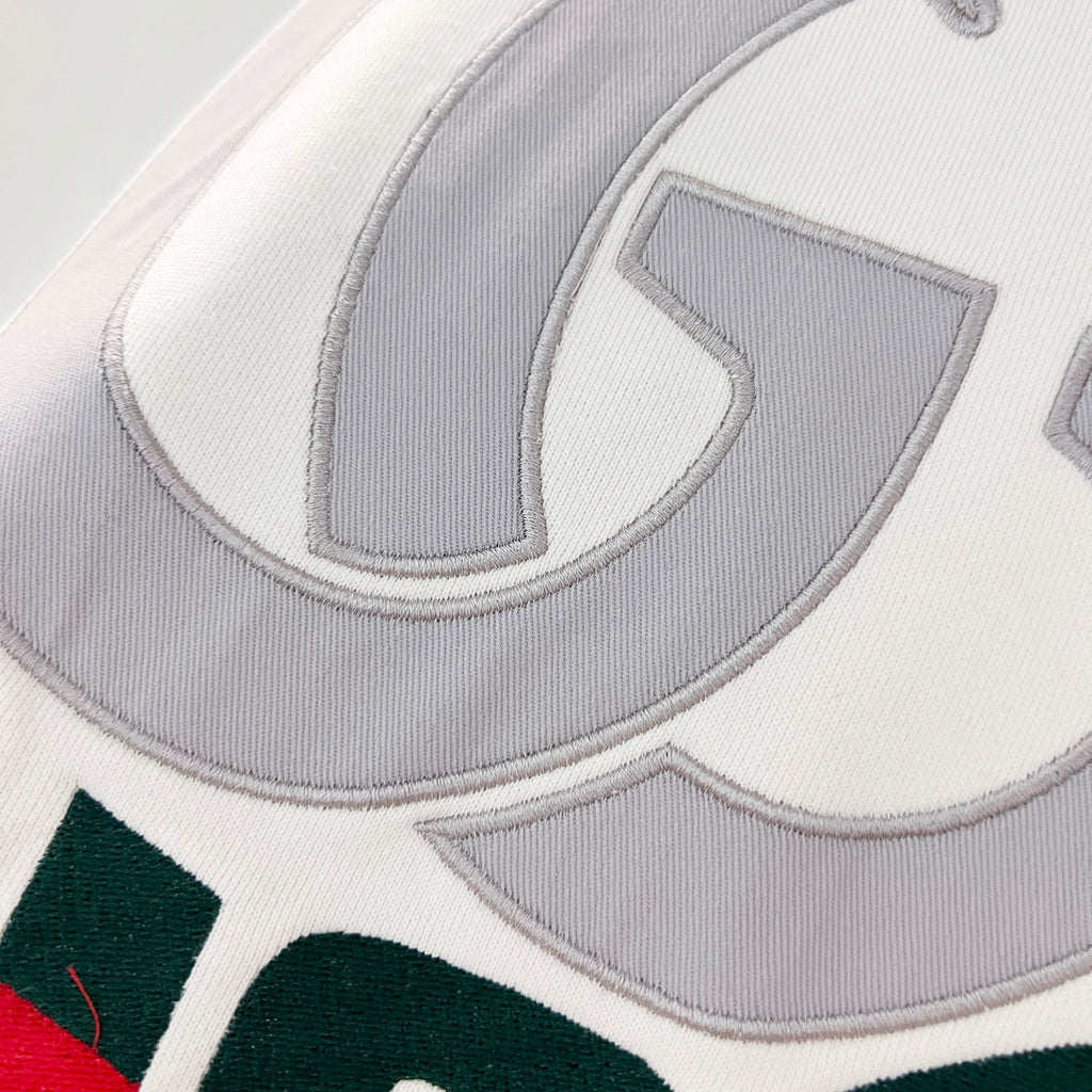 Close-up of embroidered Gucci logo on white hoodie with grey lettering