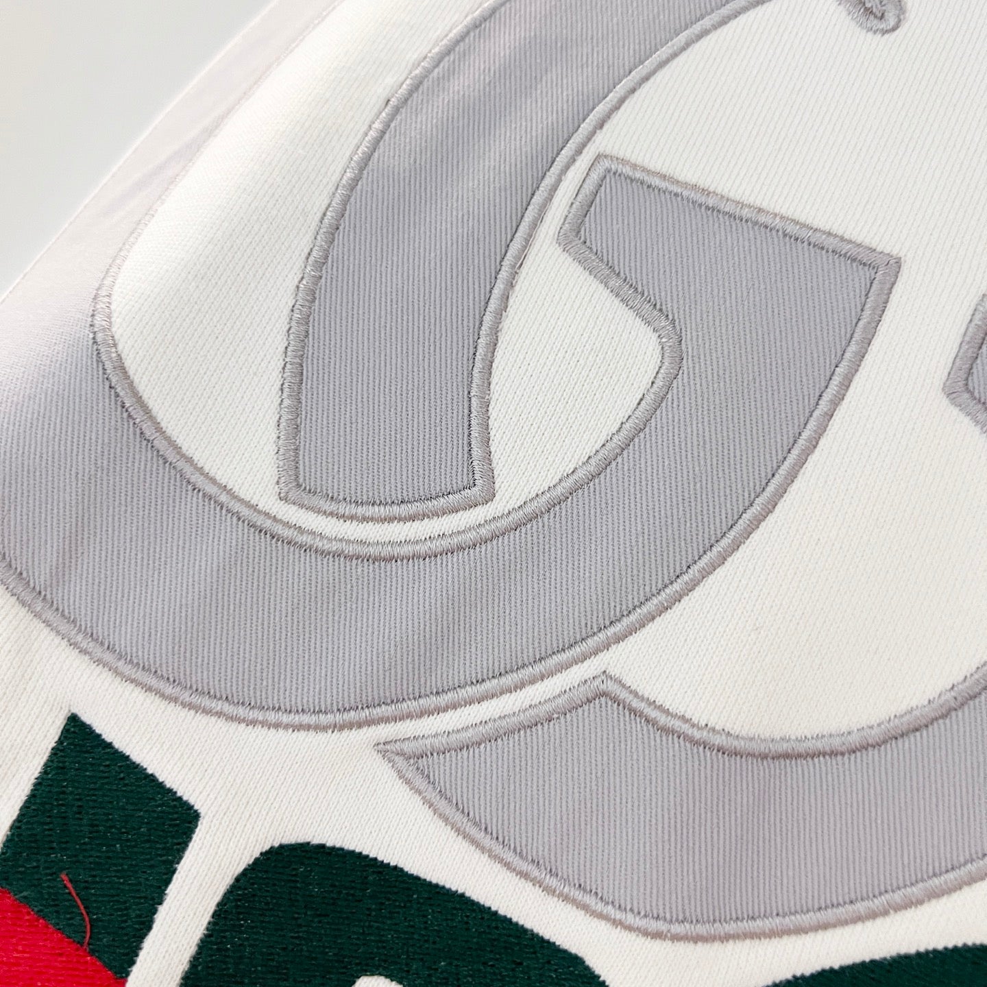 Close-up of embroidered Gucci logo on white hoodie with grey lettering