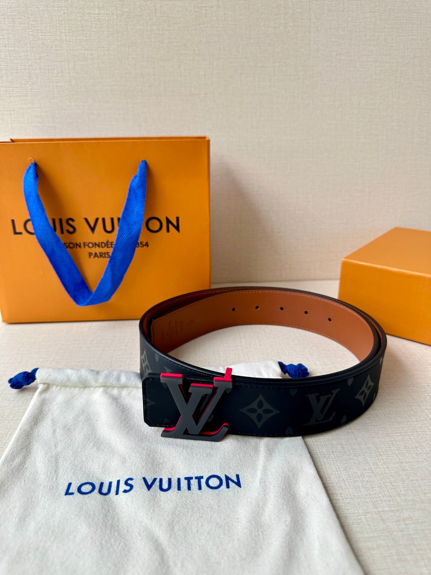 Louis Vuitton belt with dark monogram strap and red-accent LV buckle, brown back