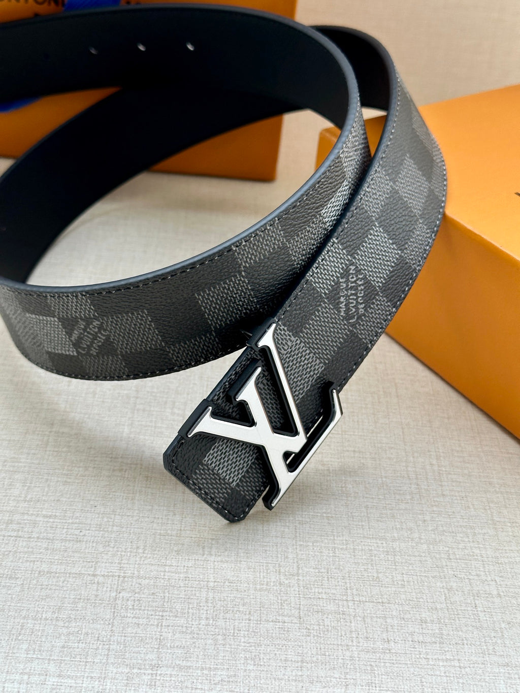 Dark gray check belt with silver LV buckle, showing black underside strap