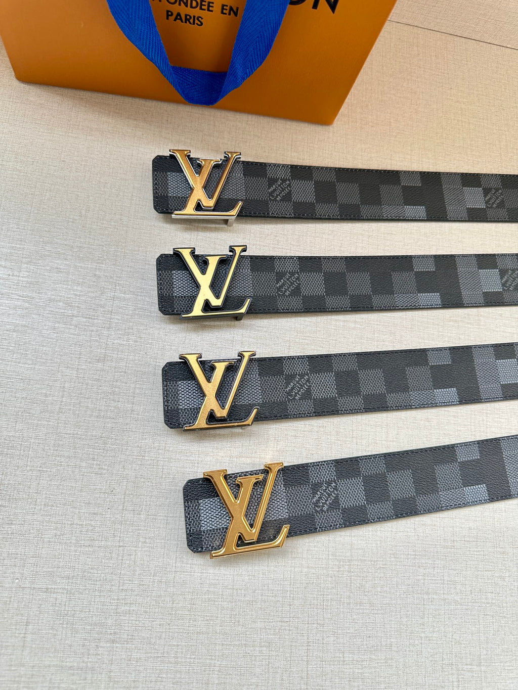 Louis Vuitton Damier belt with gold LV buckle, multiple straps on table