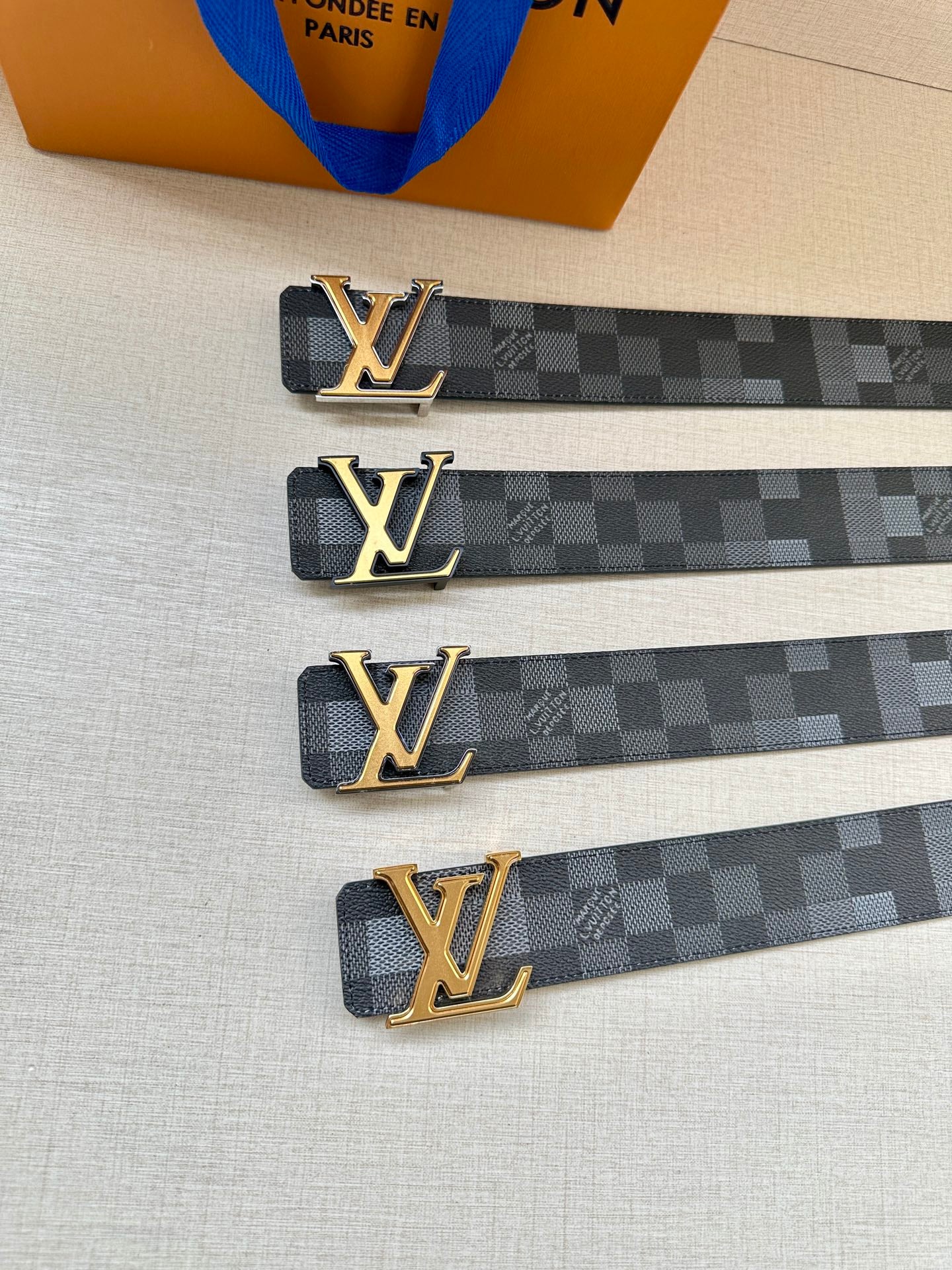 Louis Vuitton Damier belt with gold LV buckle, multiple straps on table