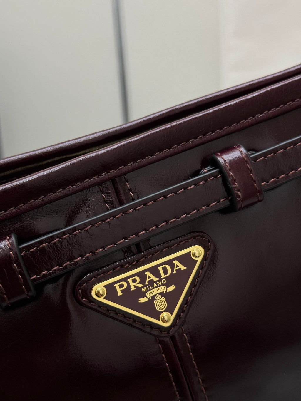 Prada burgundy leather bag close-up with gold logo badge and stitched strap details