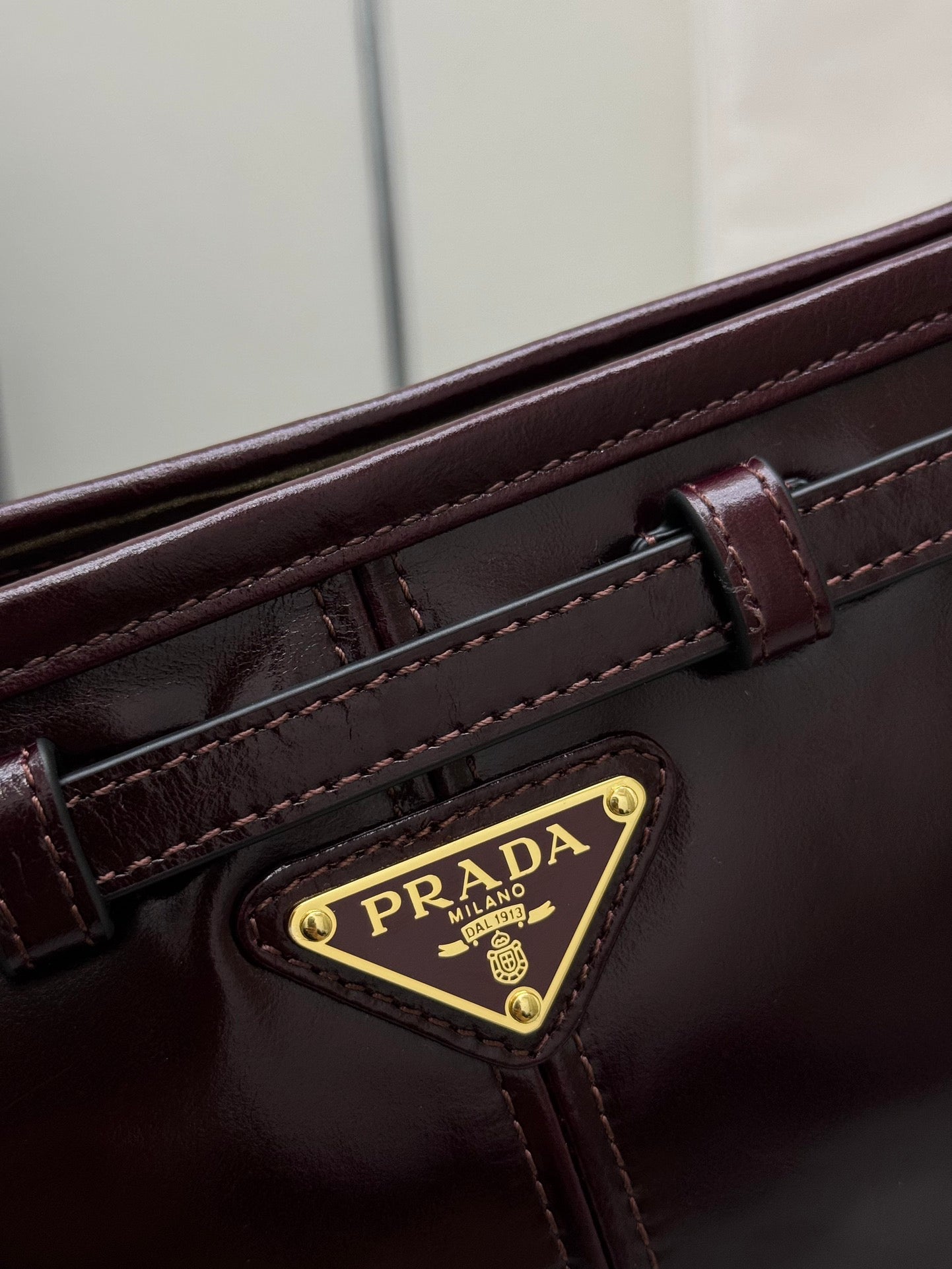 Prada burgundy leather bag close-up with gold logo badge and stitched strap details