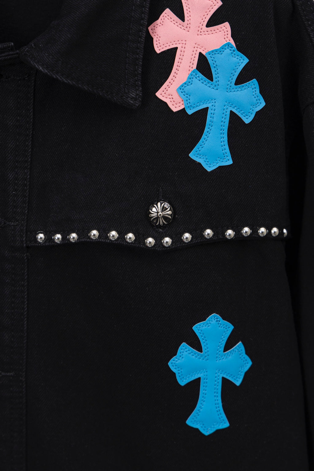 Black shirt front detail with pastel cross patches and horizontal stud band