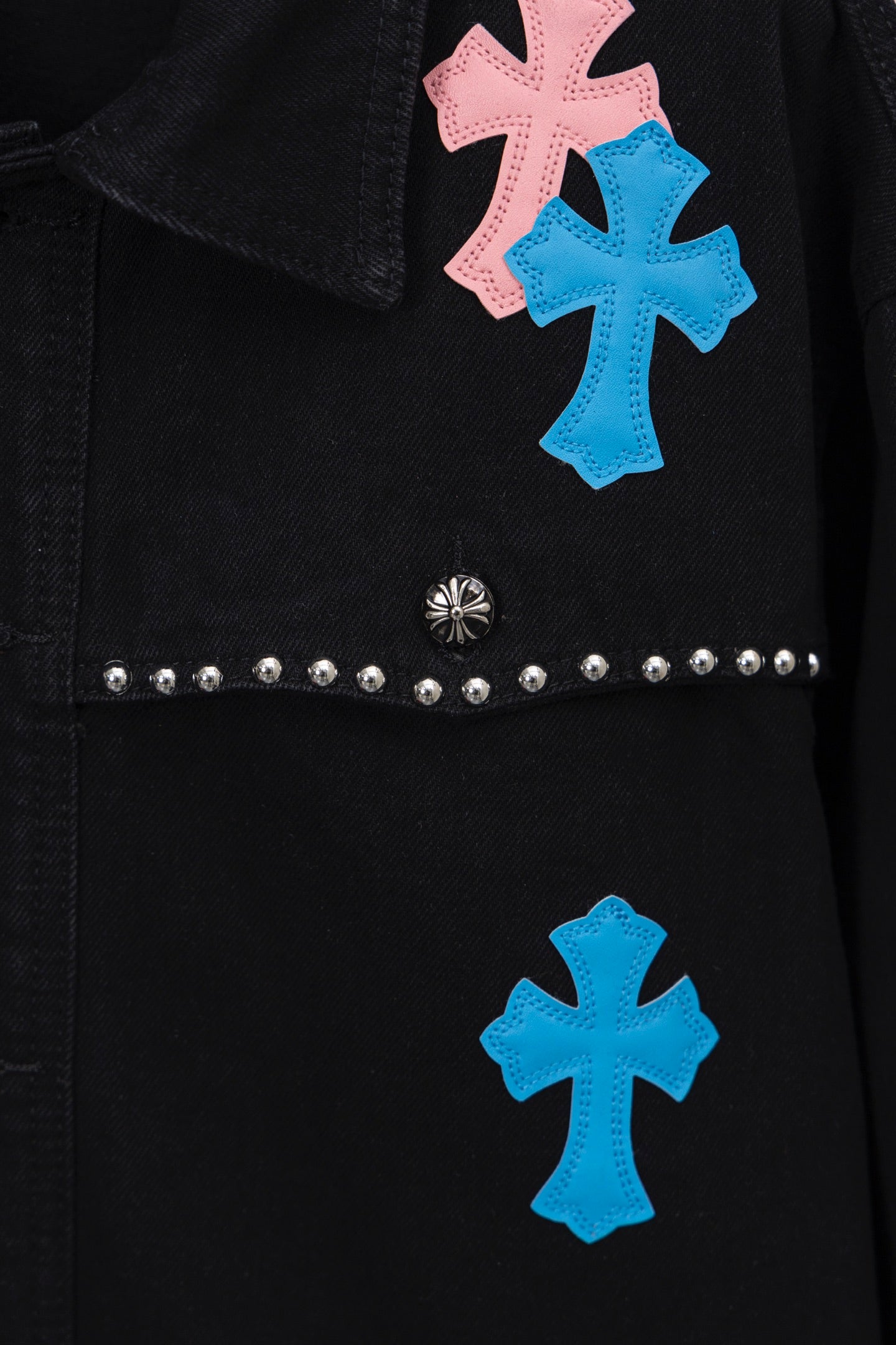 Black shirt front detail with pastel cross patches and horizontal stud band