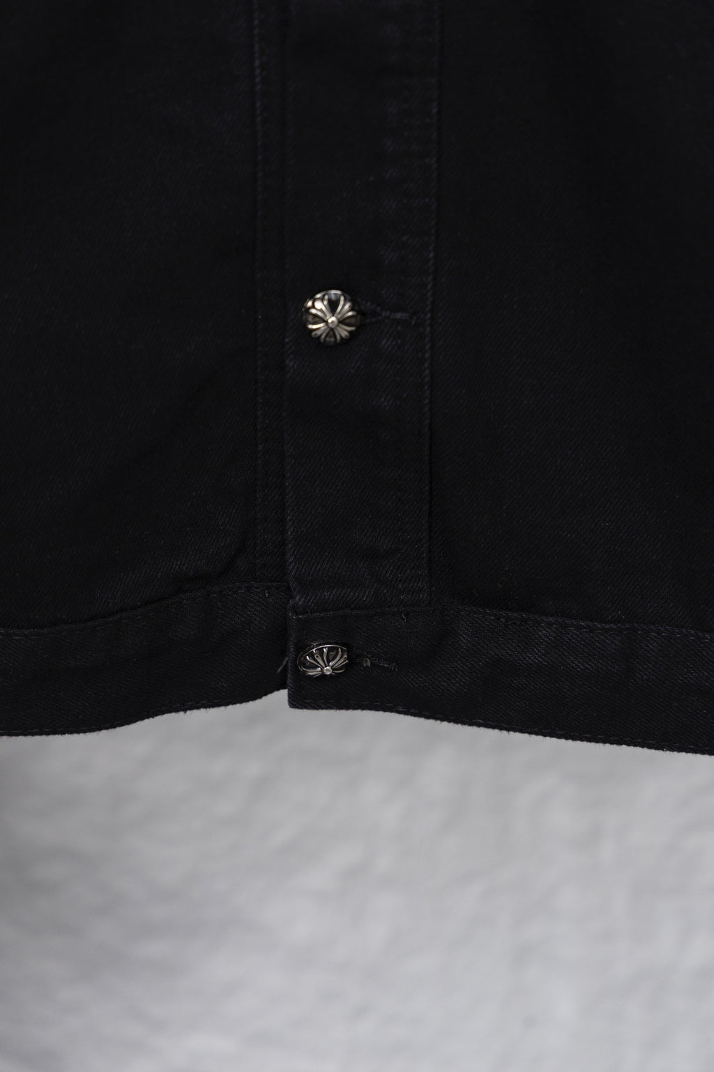 Black shirt cuff/hem with round emblem snap and stitched seam