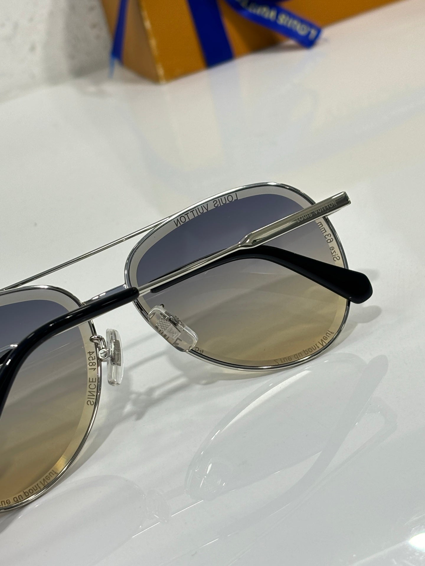 Sunglasses with silver frame and dark gradient lens, black temple and lens branding visible.