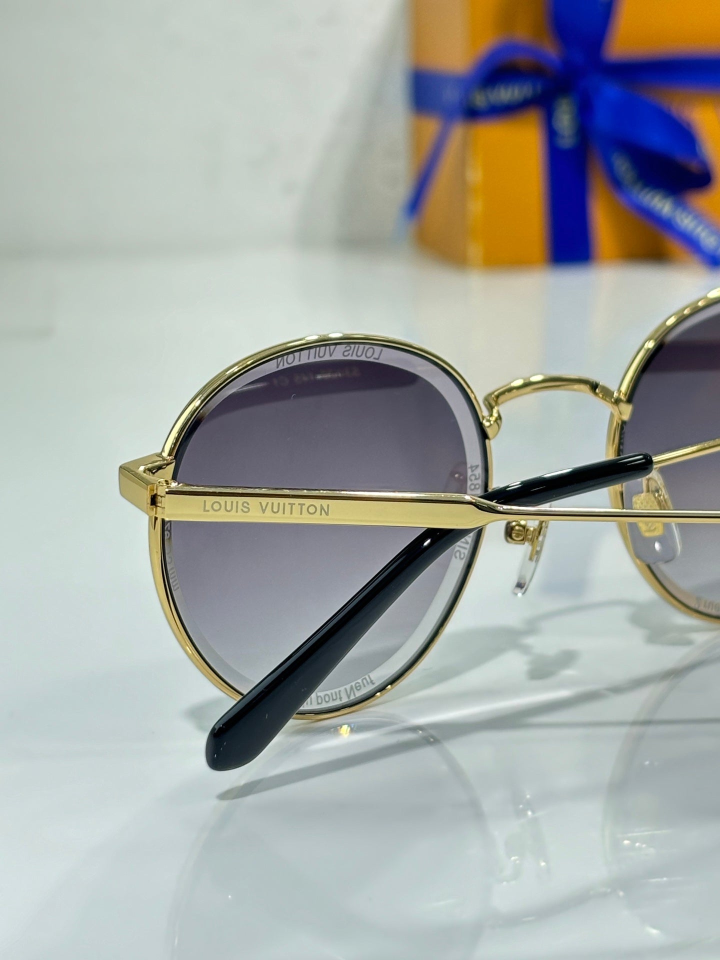 Gold-tone round sunglasses close-up with dark lens and engraved frame bar