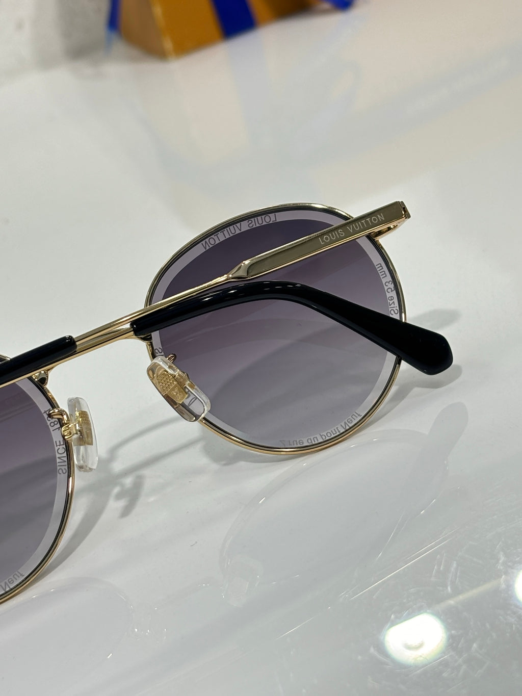 Gold-tone round sunglasses angled side view with dark lenses and black arm