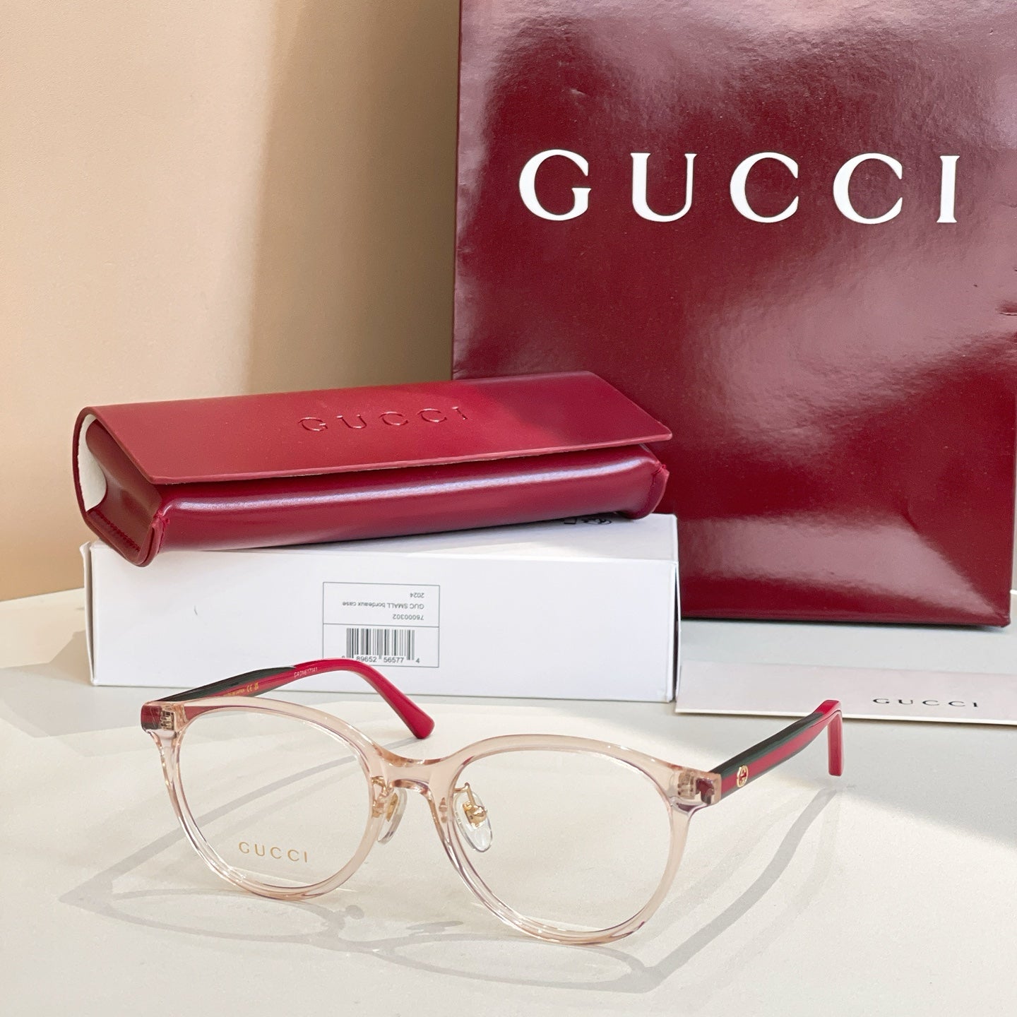 Gucci eyeglasses with light rose-gold frames and red temple tips, clear lenses