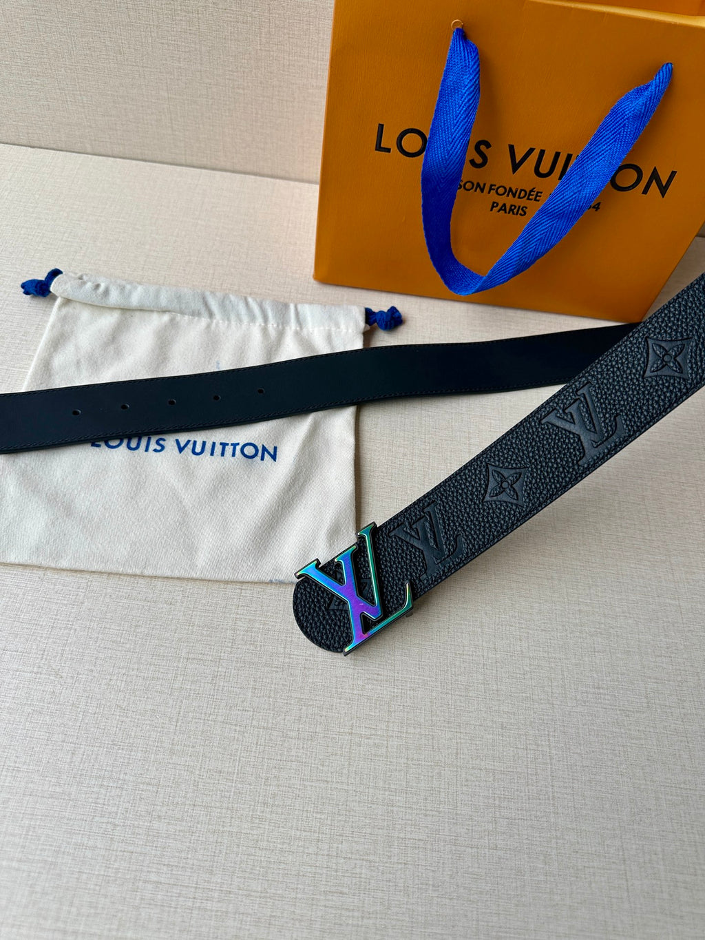 Dark leather belt with LV monogram texture and multicolor buckle laid on pouch
