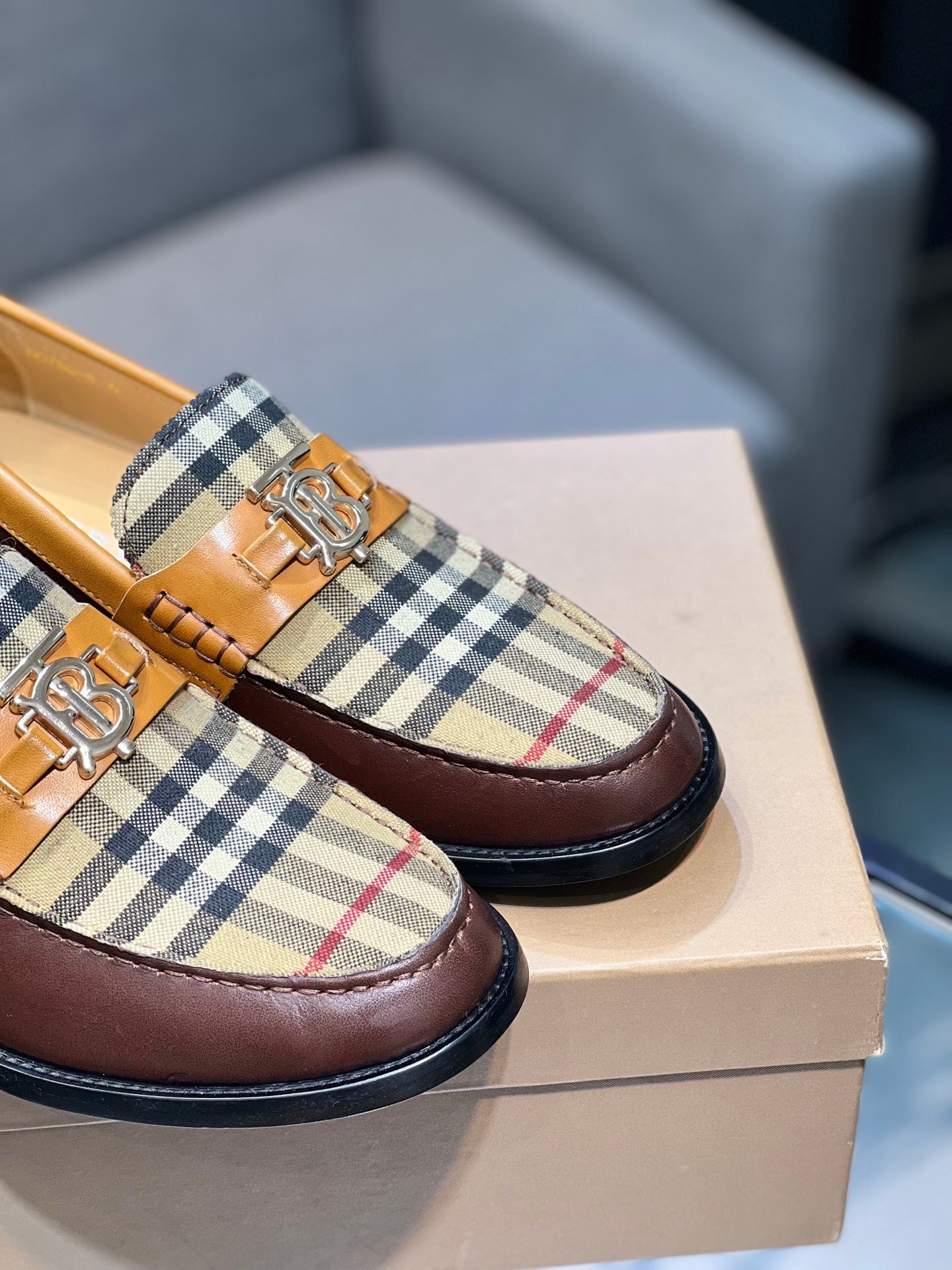 Close-up of brown loafer with tan plaid upper and gold buckle detail, angled view