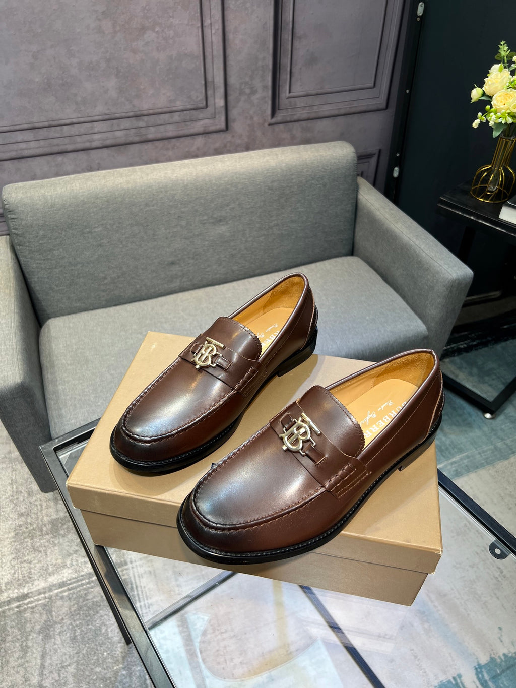 Pair of brown leather loafers with metal TB buckle and black sole on box