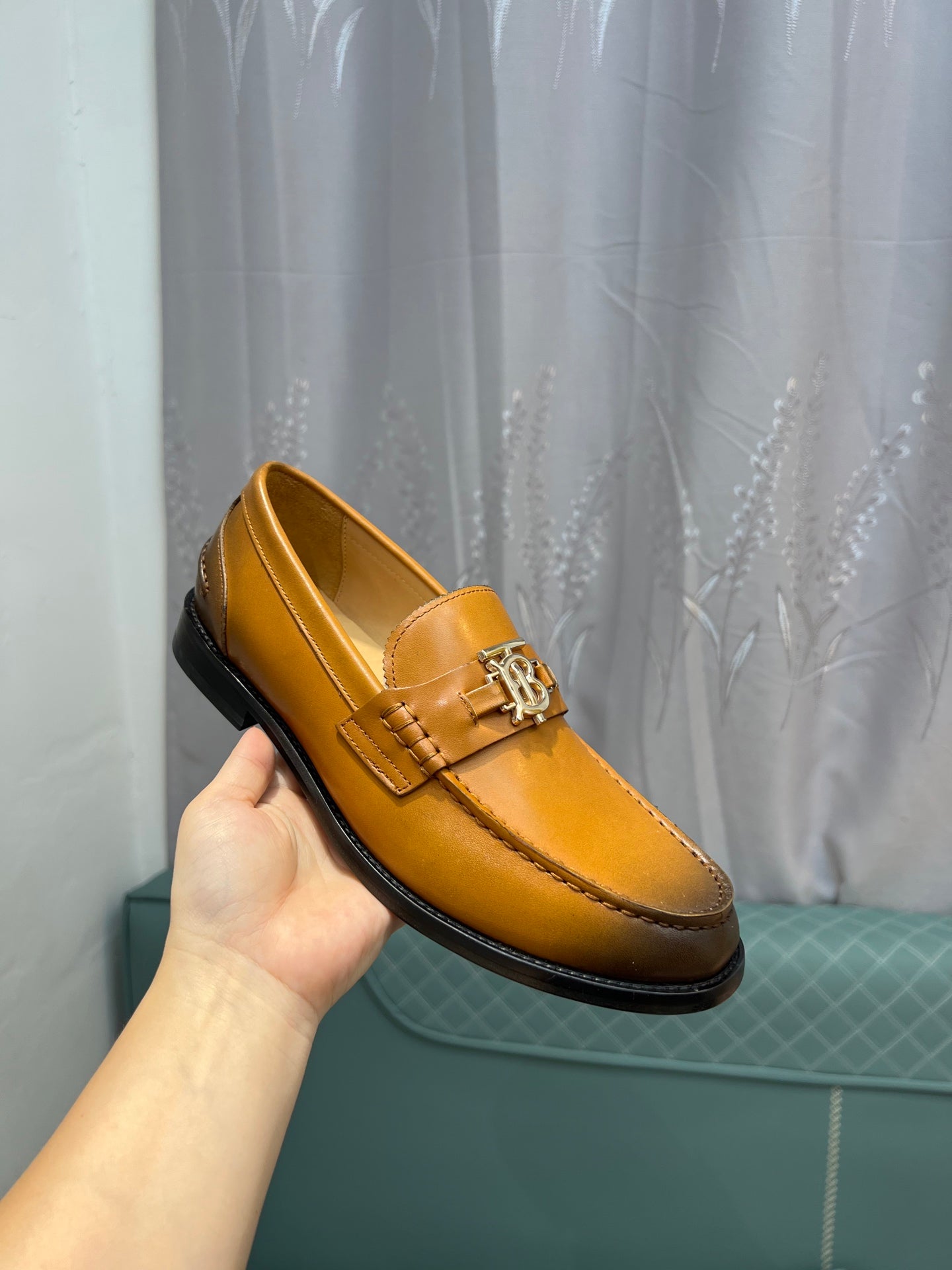 Hand holding Burberry tan leather loafer with TB metal bit and black sole