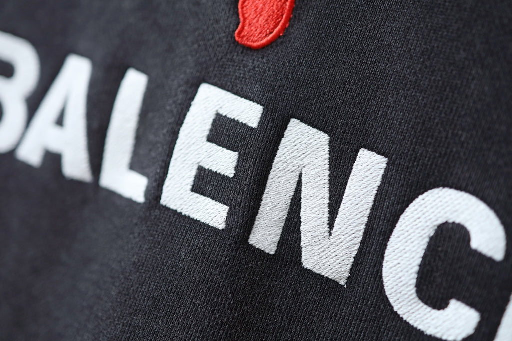 Charcoal gray hoodie fabric closeup with BALENCIAGA lettering and red puma logo