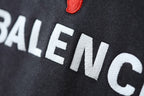 Charcoal gray hoodie fabric closeup with BALENCIAGA lettering and red puma logo