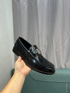 Black leather loafer held in hand, metal bit ornament and stitched edges