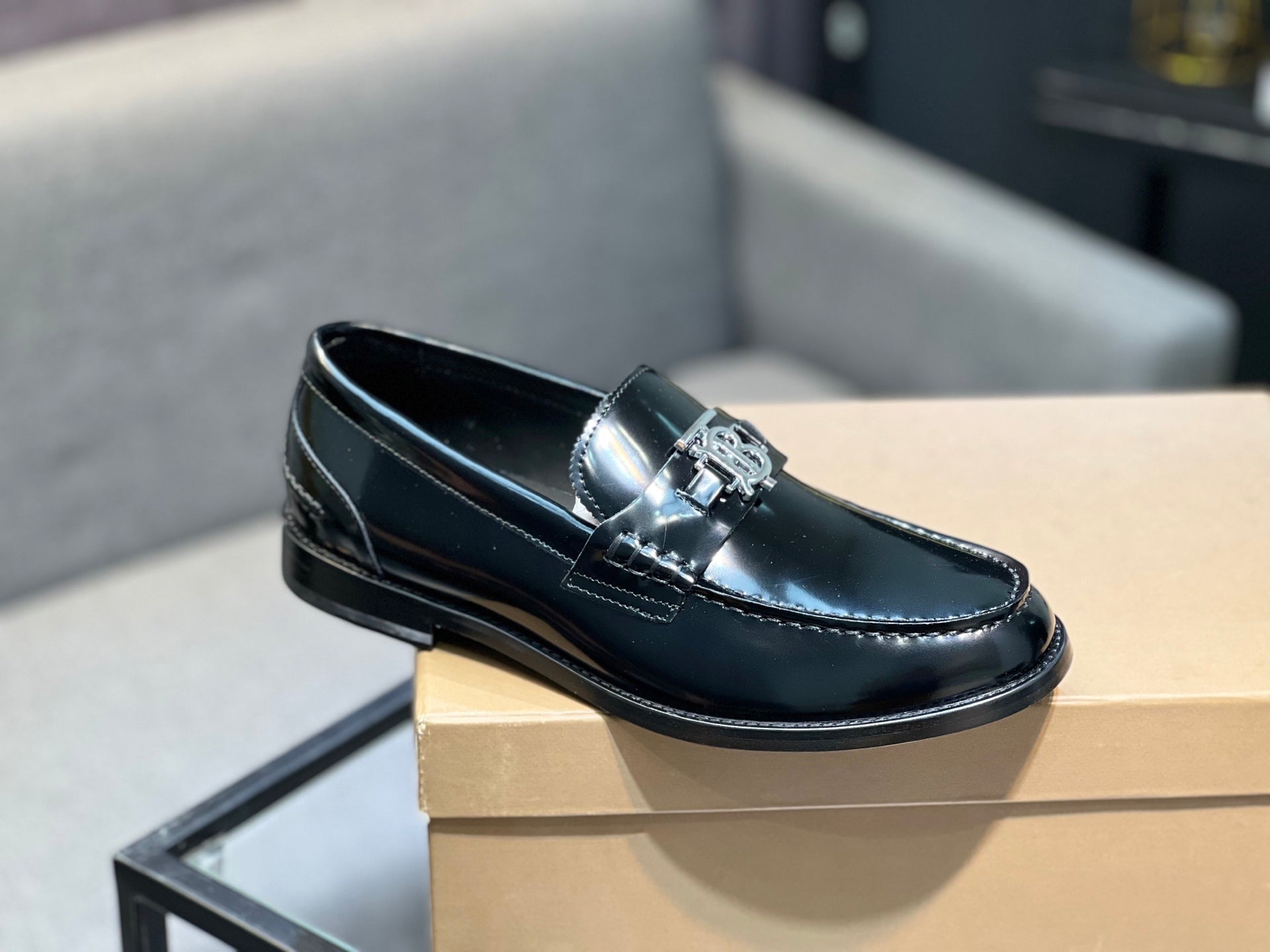Black leather loafer shoe on box, front view with metal buckle ornament