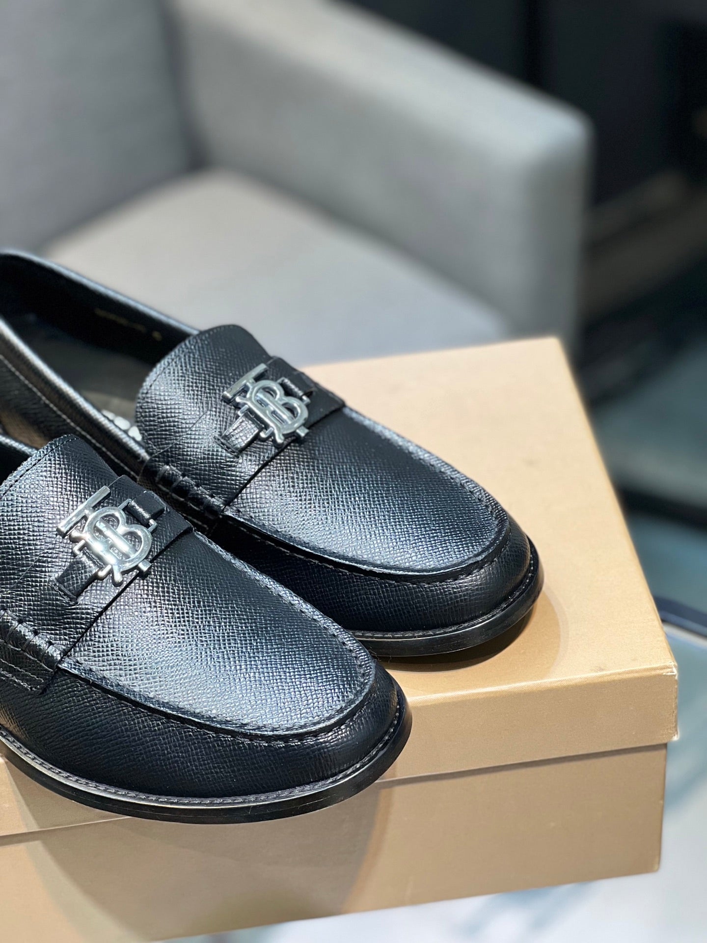 Burberry logo loafers close-up, dark leather texture with metal emblem on the vamp