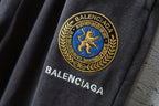 Balenciaga logo crest patch on dark fabric leg of wide-leg pants.